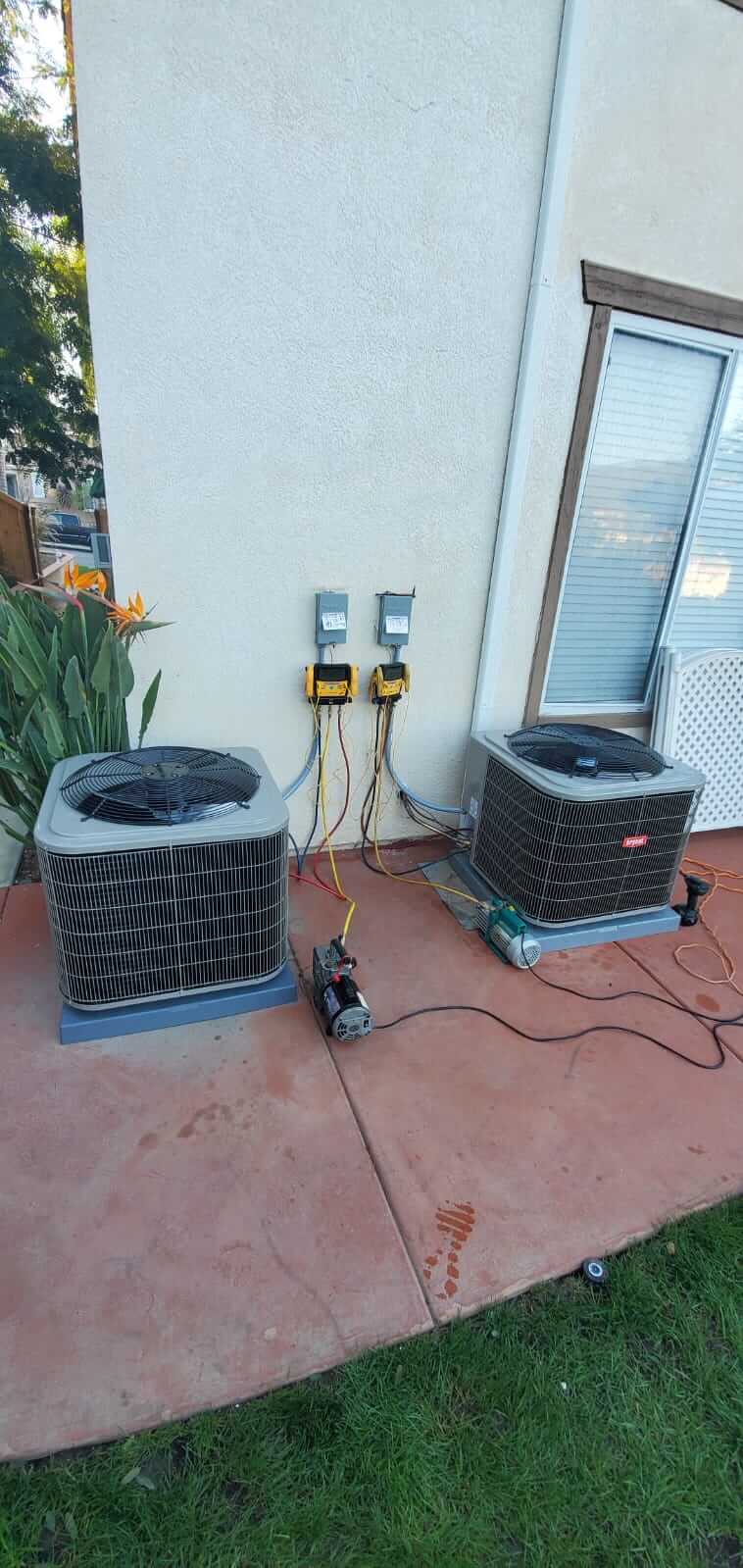 Two outdoor central air conditioning condenser units undergoing professional HVAC system diagnostics, vacuum pump testing, and pressure line evaluation by an SDAC Plumbing technician.Option
