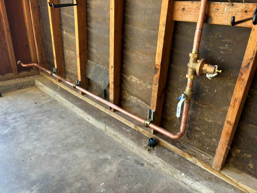 Newly installed residential copper water line piping and shutoff valves professionally routed along a garage wall framework by SDAC Plumbing.