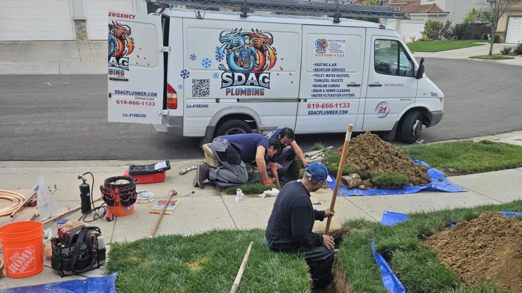 Three plumbers work together on a lawn excavation project next to an open white SDAC Plumbing service van parked on a suburban street.